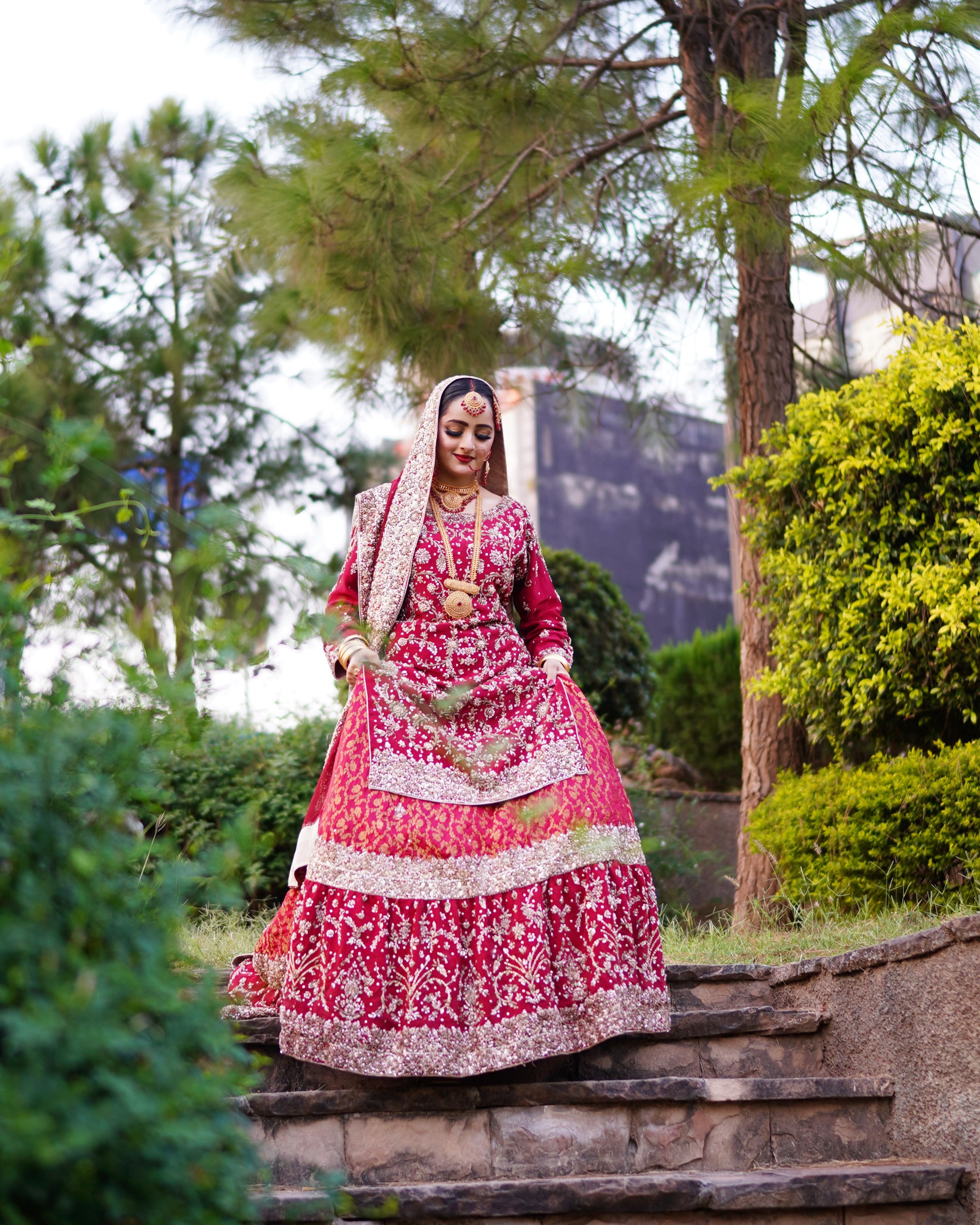 Pakistani bride in a red embroidered bridal lehenga walking down garden stairs during an outdoor wedding photoshoot captured by AM Productions.